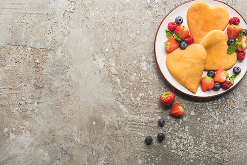 top view of heart shaped pancakes with berries on grey concrete surface