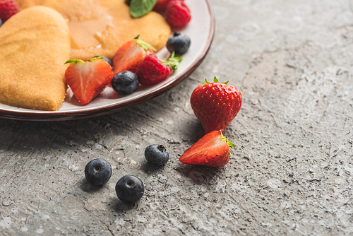 close up view of delicious heart shaped pancakes on plate near berries on grey surface