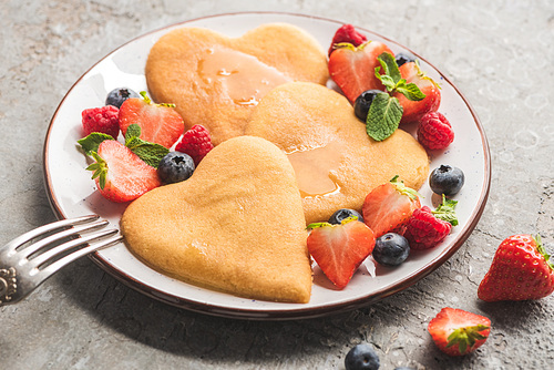 delicious heart shaped pancakes with berries on plate with fork on grey concrete surface