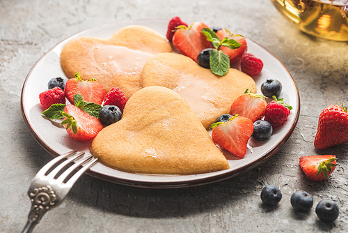 delicious heart shaped pancakes with berries on plate with fork on grey concrete surface