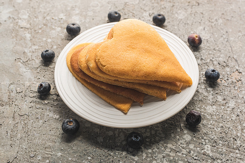 delicious heart shaped pancakes on plate near blueberries on grey concrete surface