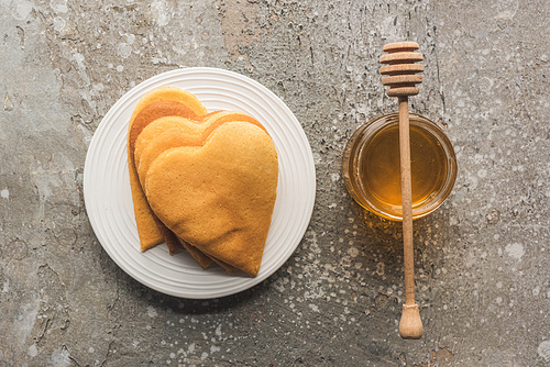 top view of heart shaped pancakes near honey on grey concrete surface