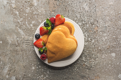 top view of heart shaped pancakes with berries on grey concrete surface