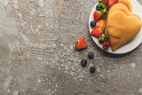 top view of heart shaped pancakes with tasty berries on plate on grey concrete surface