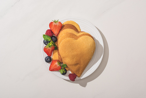top view of heart shaped pancakes with tasty berries on plate on white background