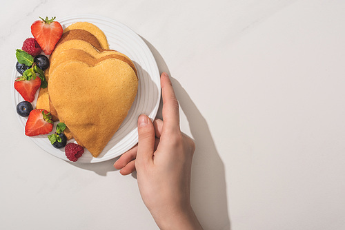 cropped view of woman holding plate with heart shaped pancakes and tasty berries on plate on white background