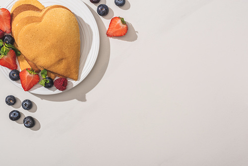 top view of heart shaped pancakes with tasty berries on plate on white background