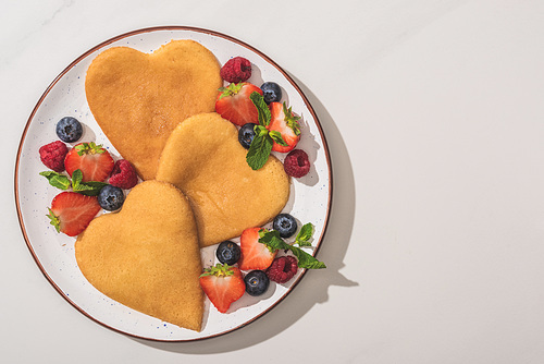 top view of tasty heart shaped pancakes with berries and mint on white background