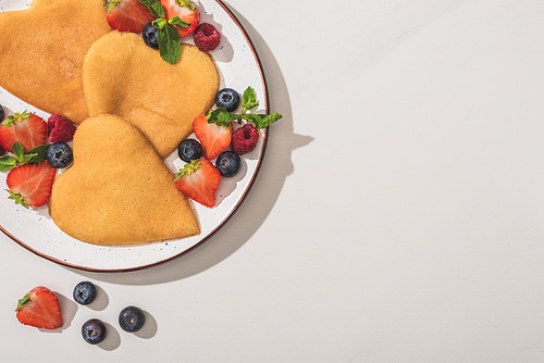 top view of tasty heart shaped pancakes with berries and mint on white background