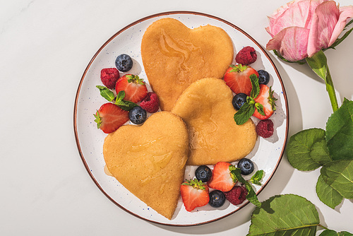 top view of delicious heart shaped pancakes with berries near rose on white background