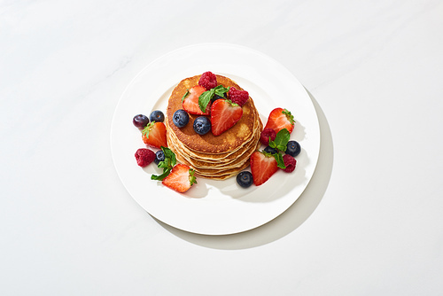 delicious pancakes with honey, blueberries and strawberries on plate on marble white surface
