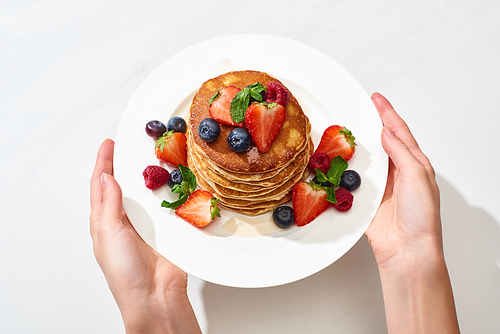 cropped view of woman holding plate with delicious pancakes with honey, blueberries and strawberries