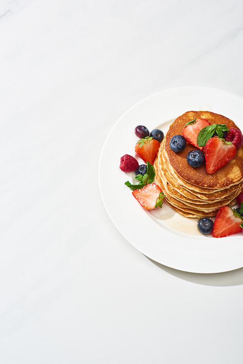 top view of delicious pancakes with honey, blueberries and strawberries on plate on marble white surface