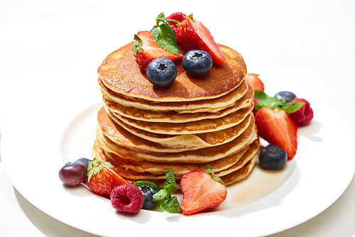delicious pancakes with honey, blueberries and strawberries on plate on white surface