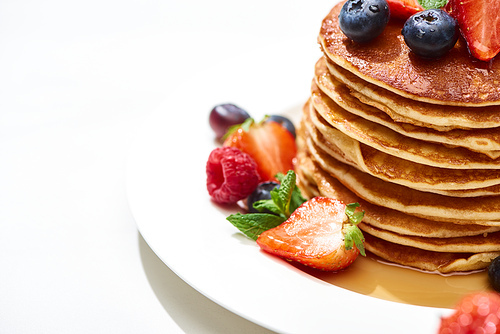 close up view of delicious pancakes with honey, blueberries and strawberries on plate on white surface