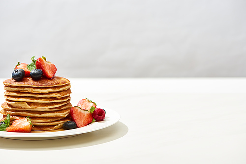 delicious pancakes with blueberries and strawberries on plate on white surface isolated on grey