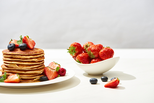 delicious pancakes with blueberries and strawberries on plate on white surface isolated on grey