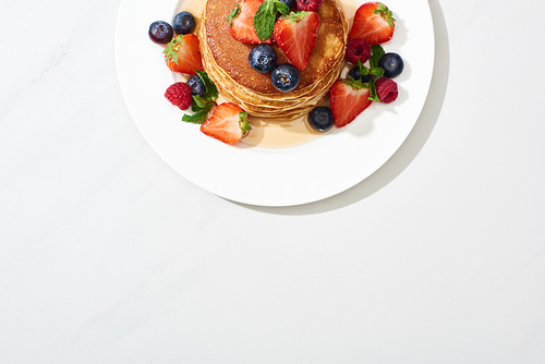 top view of delicious pancakes with honey, blueberries and strawberries on marble white surface