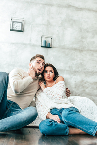 low angle view of shocked couple sitting on floor and watching movie at home