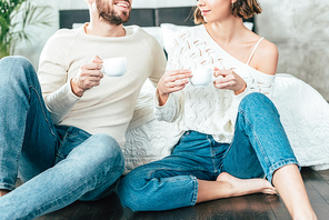 cropped view of man and woman sitting on floor and holding cups