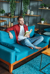 handsome man sitting on sofa and holding book in living room