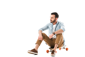 pensive bearded man sitting on longboard and looking away isolated on white