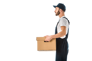 side view of delivery man in overalls and cap holding cardboard box isolated on white