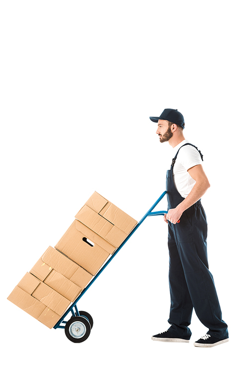 serious delivery man transporting hand truck loaded with cardboard boxes isolated on white