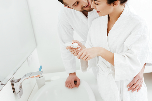 cropped view of bearded man looking at girlfriend holding toothpaste in bathroom