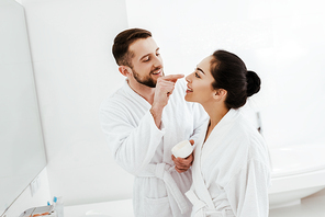 cheerful man applying face cream on nose of attractive girlfriend