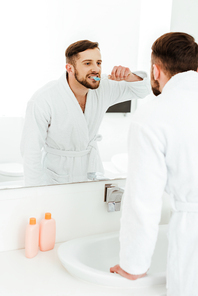 selective focus of handsome man brushing teeth while looking at mirror in bathroom