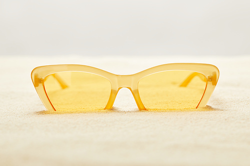 selective focus of yellow sunglasses in golden sand isolated on grey