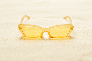 selective focus of yellow sunglasses in sandy beach in summer