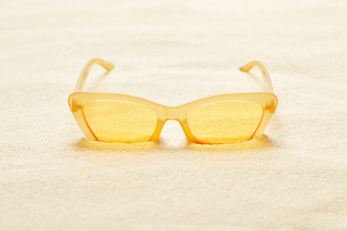 selective focus of yellow sunglasses in sandy beach in summer