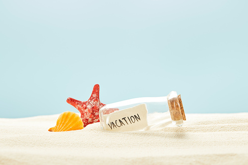 glass bottle with vacation lettering on paper near seashell and starfish isolated on blue