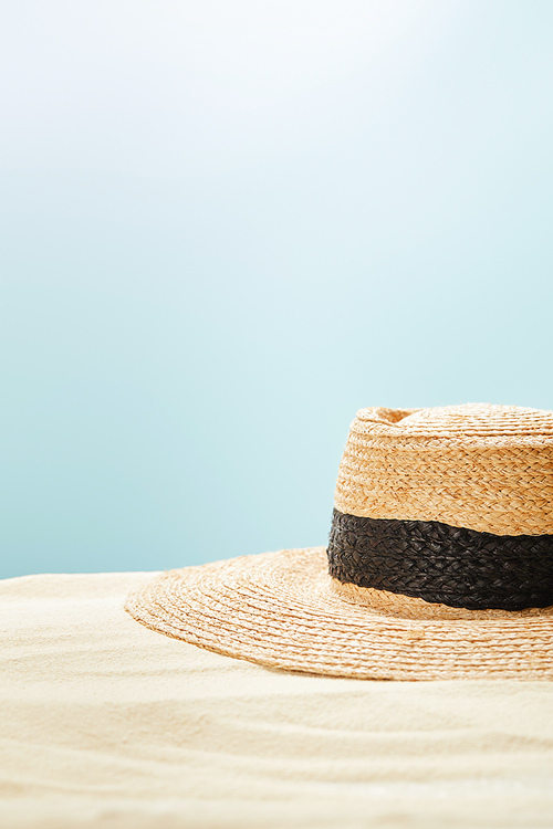 selective focus of straw hat on golden sand in summertime isolated on blue