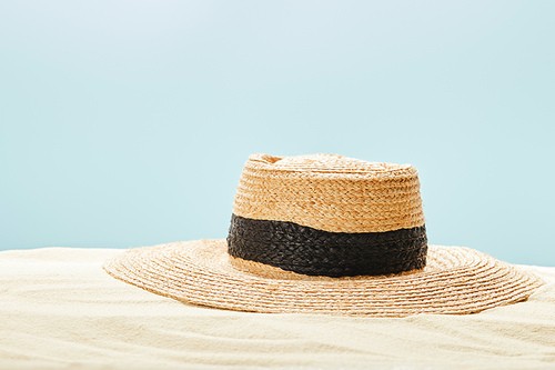 selective focus of straw hat on sandy beach in summertime isolated on blue