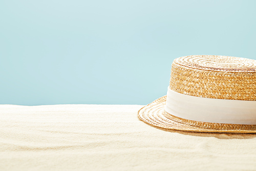 selective focus of straw hat on sandy beach in summertime isolated on blue