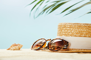 selective focus of sunglasses near straw hat and seashell in summertime isolated on blue