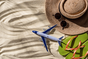 top view of toy plane, straw hat, flip flops and sunglasses on wavy sand with copy space