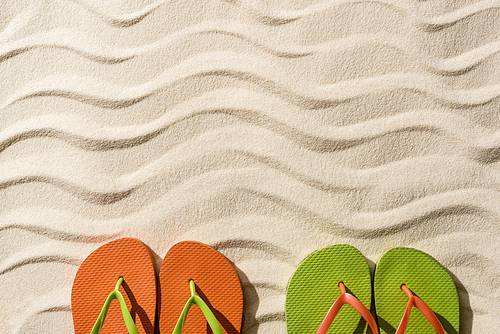 top view of colorful flip flops on wavy sand with copy space