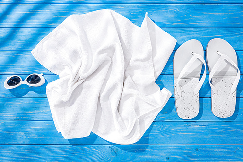 top view of White crumpled towel, sunglasses and flip flops on blue wooden background