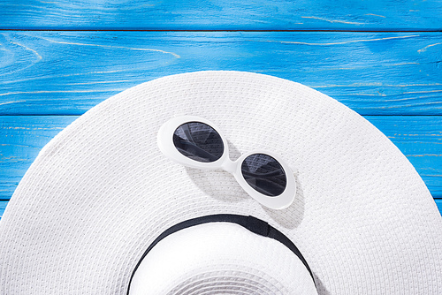 top view of white sunglasses and white floppy hat with black ribbon on blue wooden background
