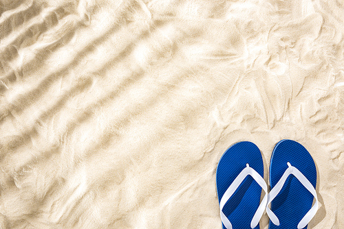 top view of white blue flip flops on sand with shadows and copy space