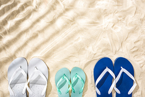 top view of white, turquoise and white blue flip flops on sand with shadows and copy space