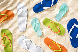 top view of scattered white, turquoise, green and blue flip flops on sand with shadows