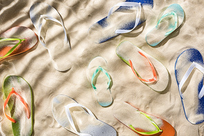 top view of scattered turquoise, orange, blue and green flip flops on sand with shadows