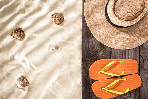 top view of orange flip flops and straw hat with black ribbon on wooden board and sand with seashells and copy space