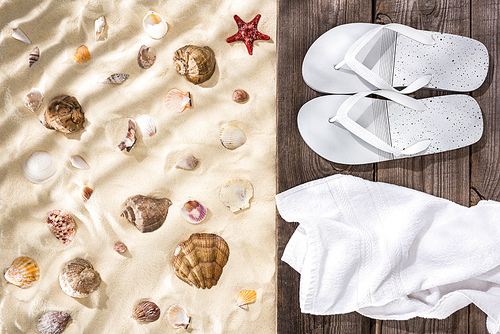 top view of seashells and starfish on sand and flip flops and white towel on wooden brown board
