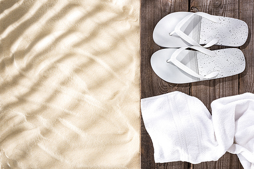Top view of white flip flops and towel on wooden brown board and sand with copy space